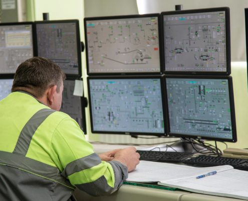 A male engineer, in special clothing, sits against the background of monitors