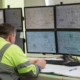 A male engineer, in special clothing, sits against the background of monitors