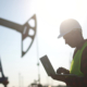 oil business. a worker works next to an oil pump holding a laptop
